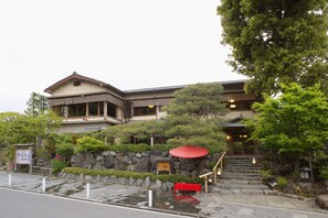 A traditional Japanese building with a stone wall, a red umbrella, and a staircase leading to the entrance. - Arashiyama Benkei (Kyoto)