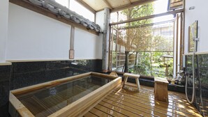 A traditional Japanese onsen with a wooden deck, a large hot spring bath, and a view of greenery outside. - Arashiyama Benkei (Kyoto)