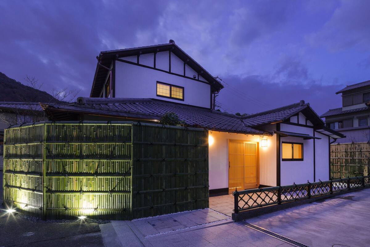 Uma casa tradicional japonesa com cerca de madeira, telhado de telhas e pequeno alpendre.