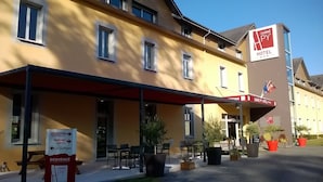 A hotel with a reception area, outdoor seating, and a sign indicating the hotel name. - Carré Py' Hôtel (Bagnères-de-Bigorre)