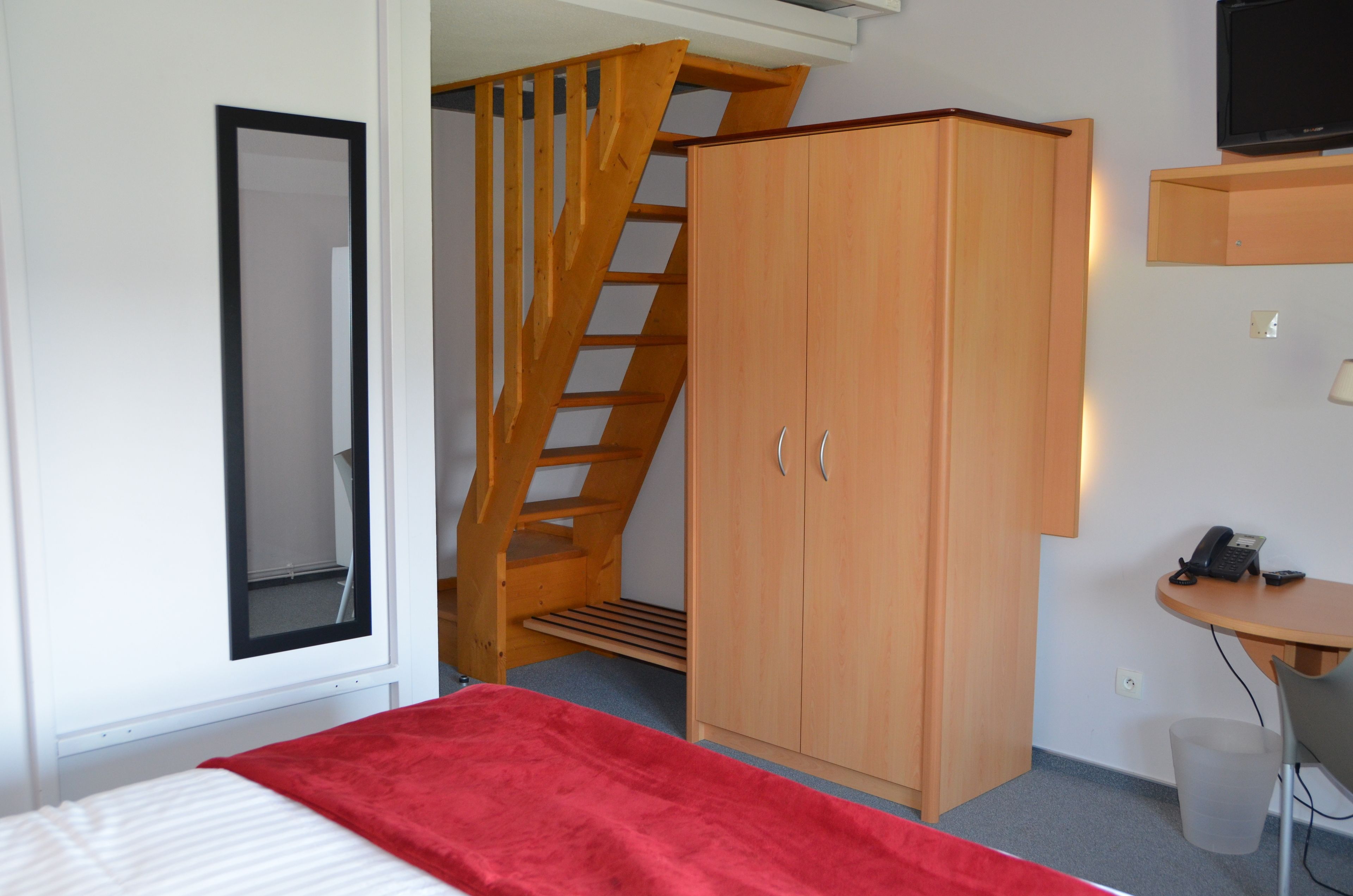Un dormitorio con cama, armario, escritorio con teléfono y televisor montado en la pared.