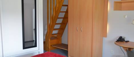 A bedroom with a bed, a wardrobe, a desk with a telephone, and a television mounted on the wall.