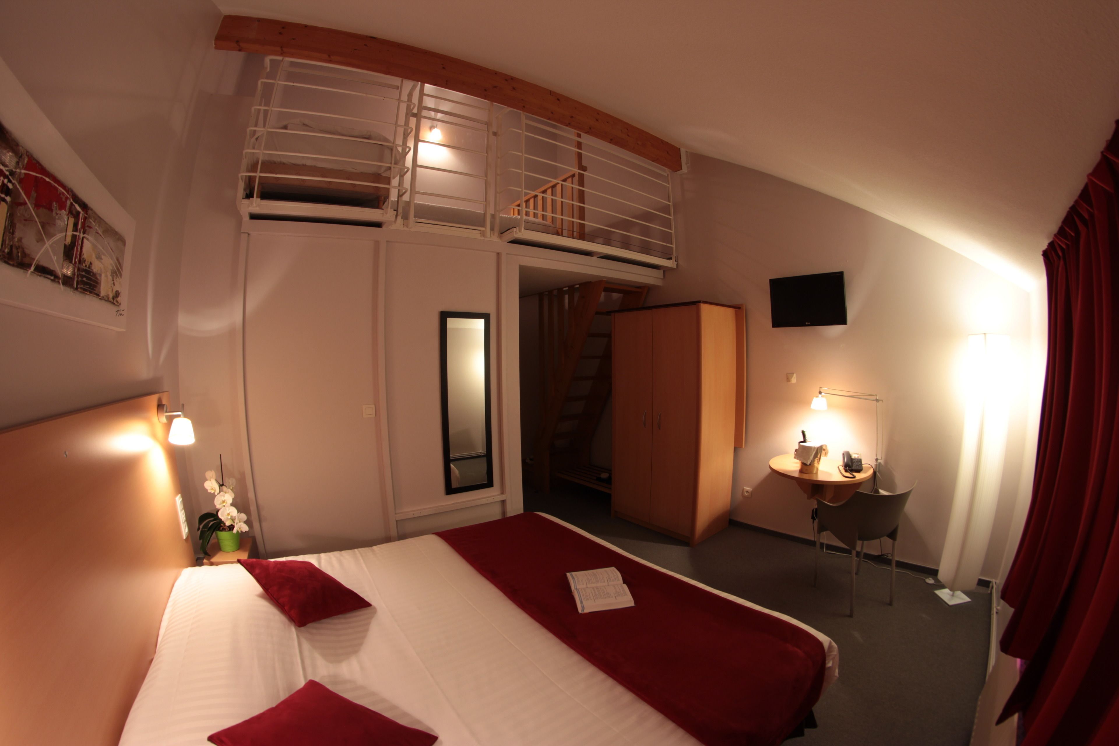 A hotel room with a bed, a desk, a chair, a TV, and a staircase.