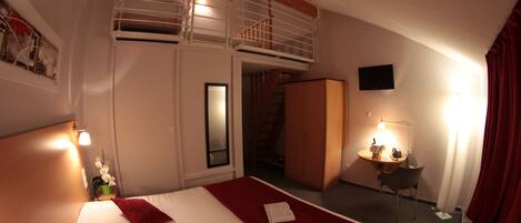 A hotel room with a bed, a desk, a chair, a TV, and a staircase.