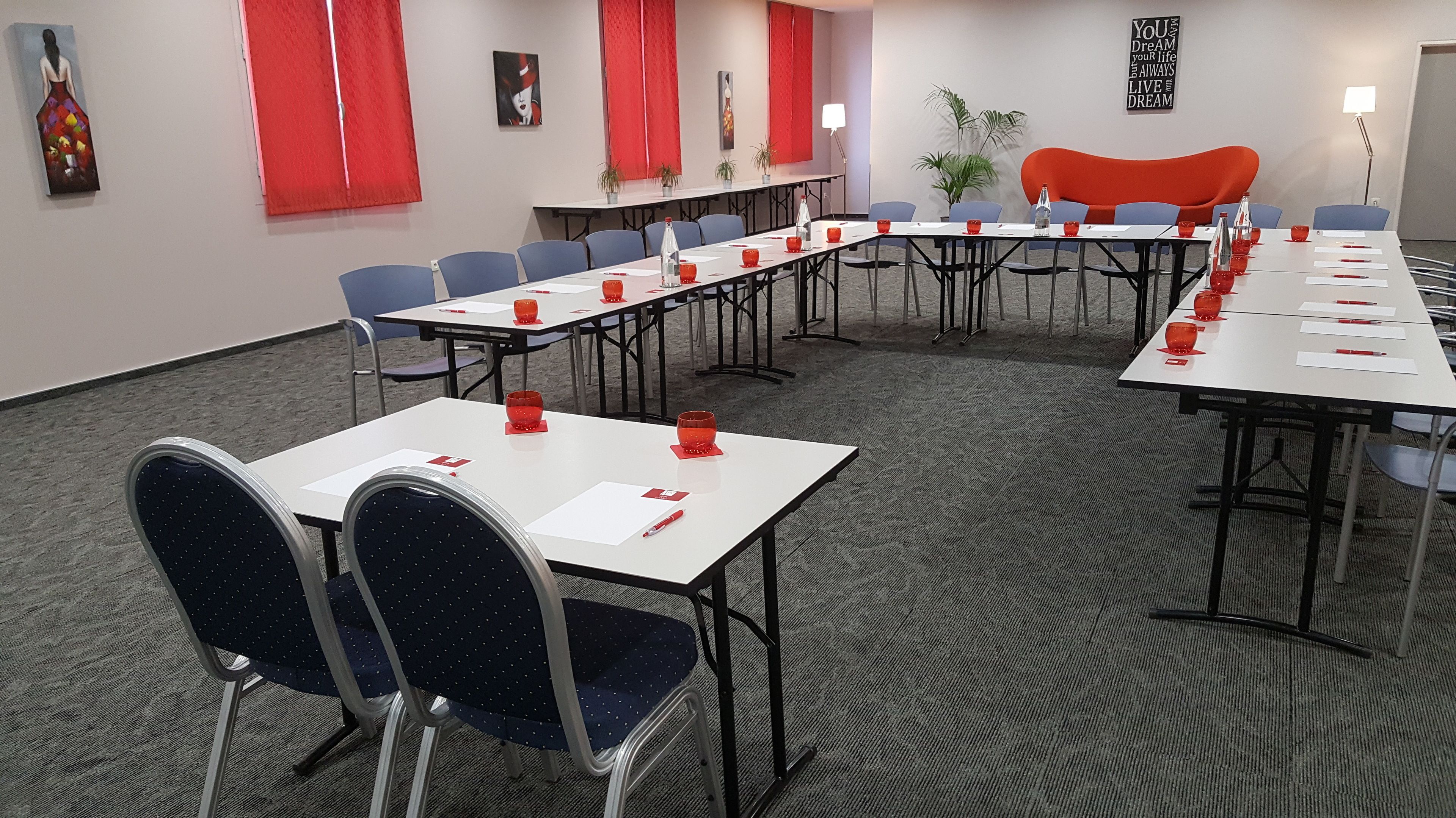 Une salle de conférence avec des tables blanches, des dessous de verre rouges et des chaises bleues.