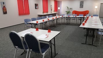 Une salle de conférence avec des tables blanches, des dessous de verre rouges et des chaises bleues.