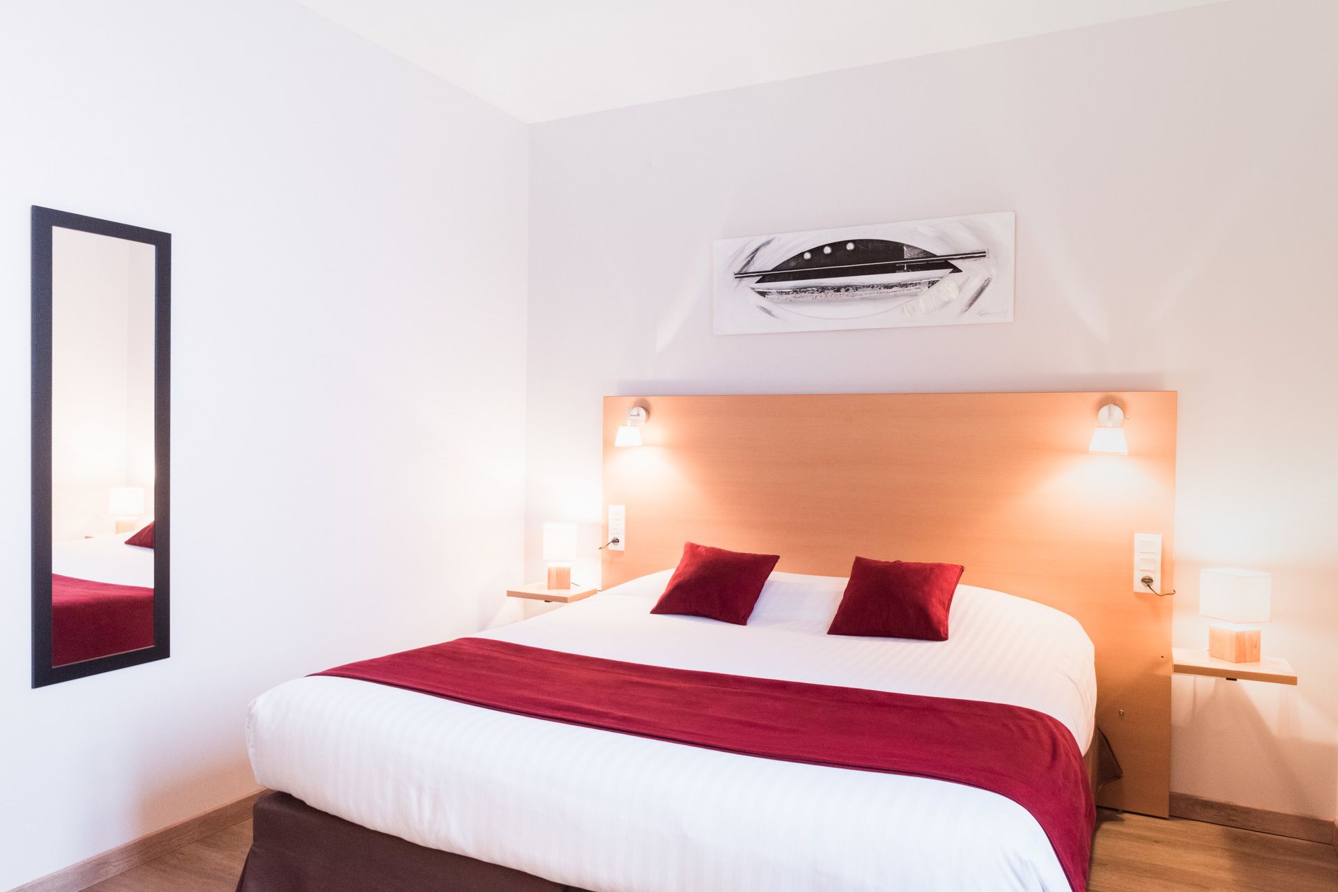 Une chambre d’hôtel avec un grand lit, des oreillers rouges, une tête de lit en bois et des lampes fixées au mur.