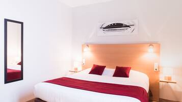 Une chambre d’hôtel avec un grand lit, des oreillers rouges, une tête de lit en bois et des lampes fixées au mur.