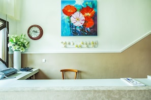 A reception desk with a clock, a vase of flowers, and a painting of red flowers on the wall. - Lemon Garden Villa (Kassandra)