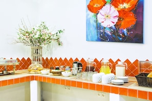A breakfast bar with orange tiles, a vase of branches, and a painting of flowers. - Lemon Garden Villa (Kassandra)