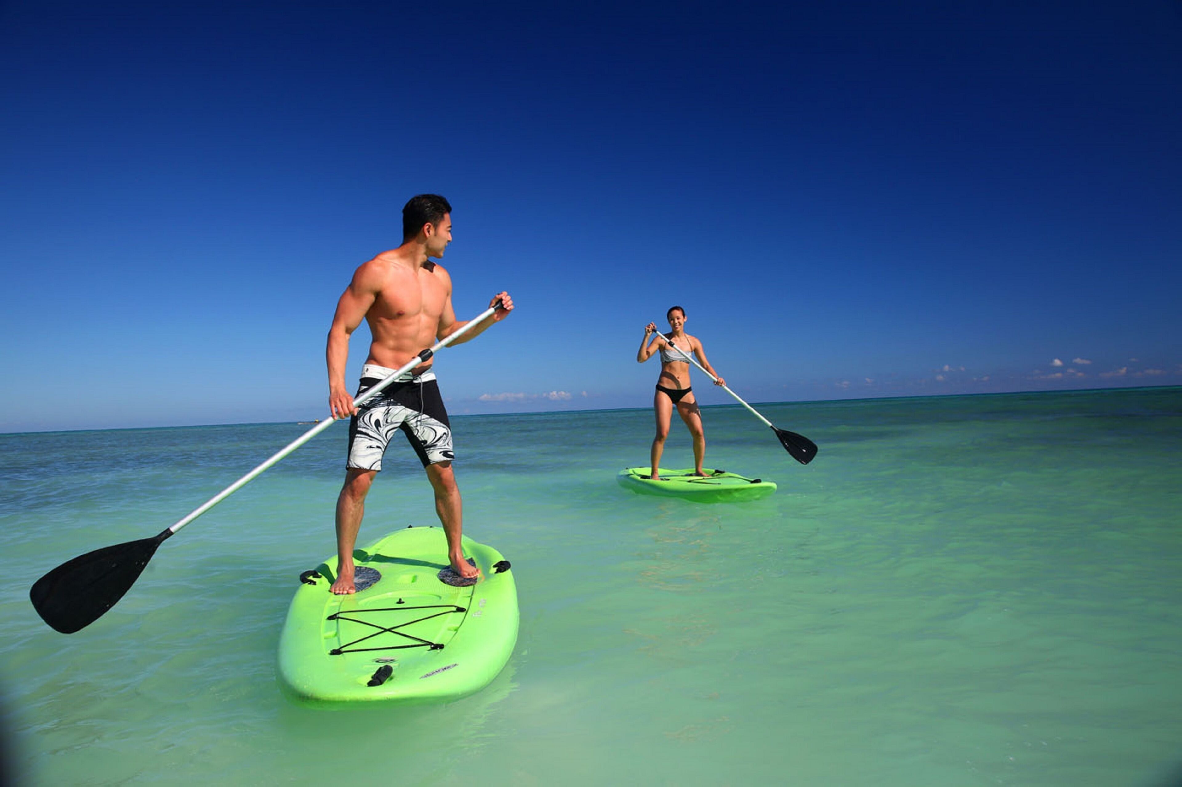 Two people paddleboarding on a clear turquoise sea with a clear sky.
