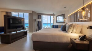A modern hotel room with a large bed, a TV, and a view of the ocean.