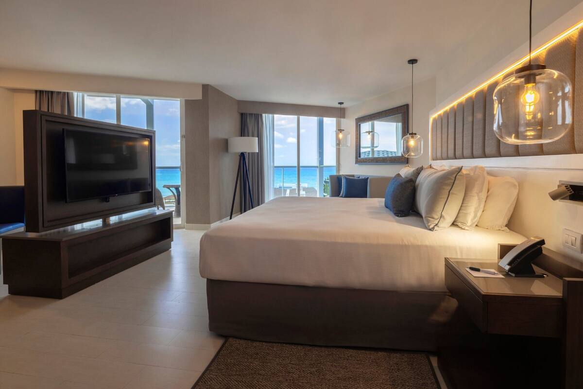 A modern hotel room with a large bed, a TV, and a view of the ocean.