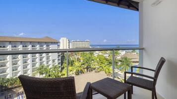 A balcony with wicker furniture, a view of a hotel building, and a beach in the background.