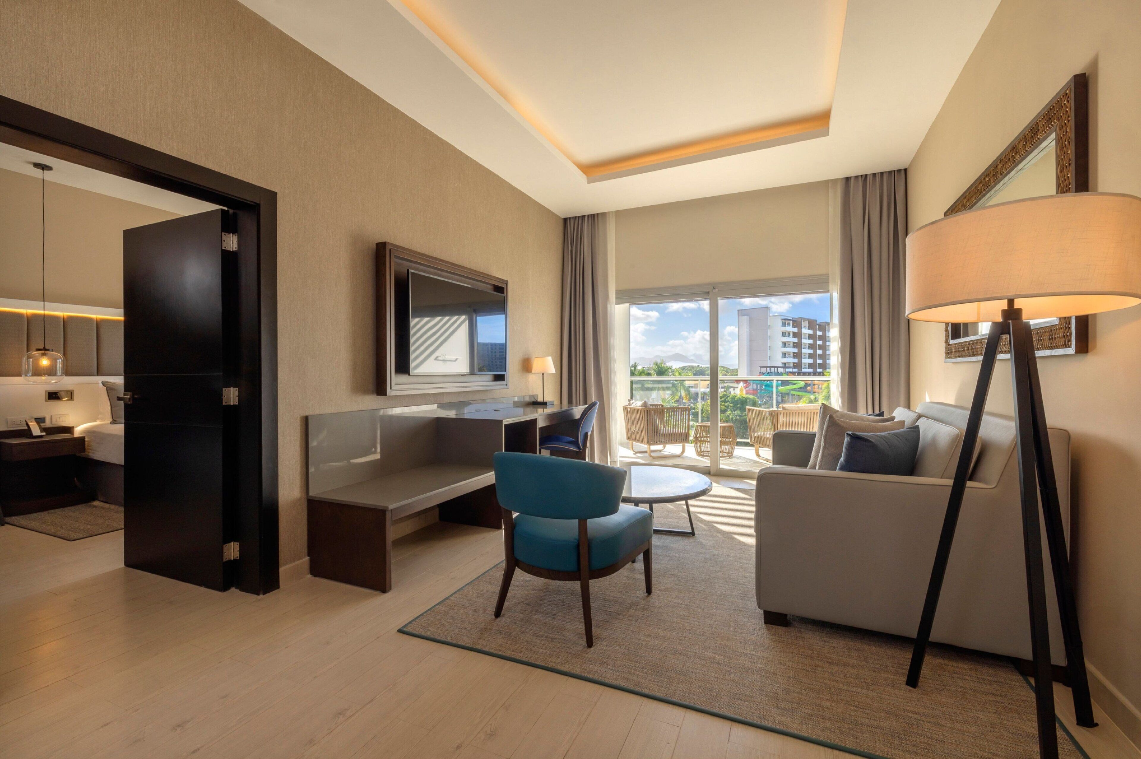 Quarto de hotel moderno com sofá, poltrona e televisão de tela plana.