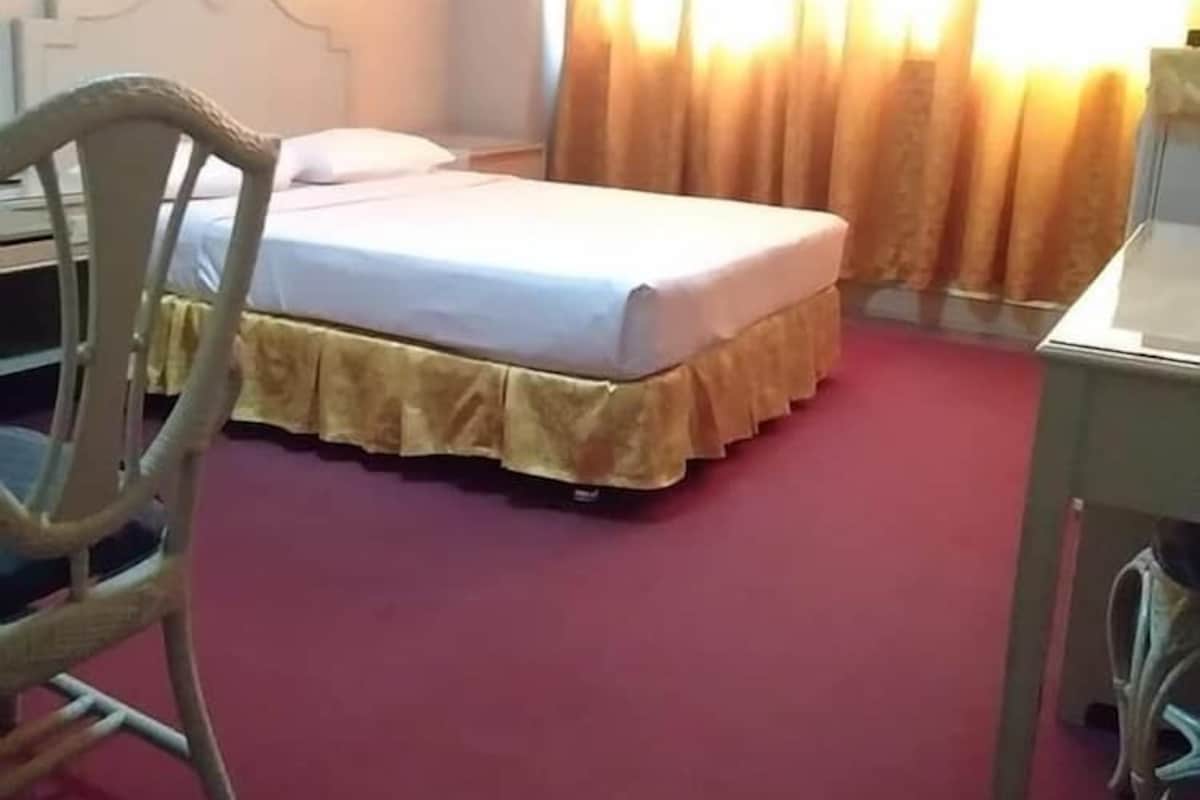 A hotel room with a bed, a chair, a desk, and a window with curtains.