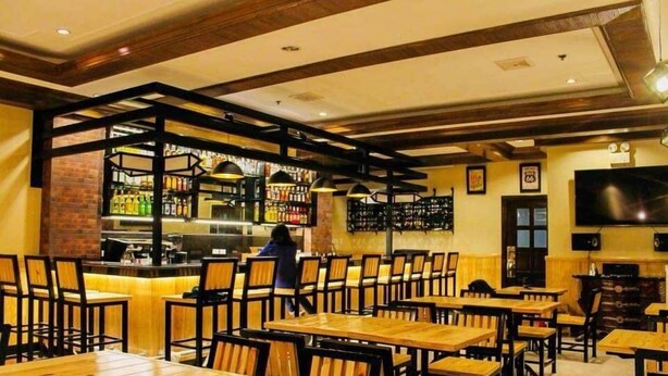 Un restaurant avec des tables et des chaises en bois, un coin bar et un écran de télévision fixé au mur.