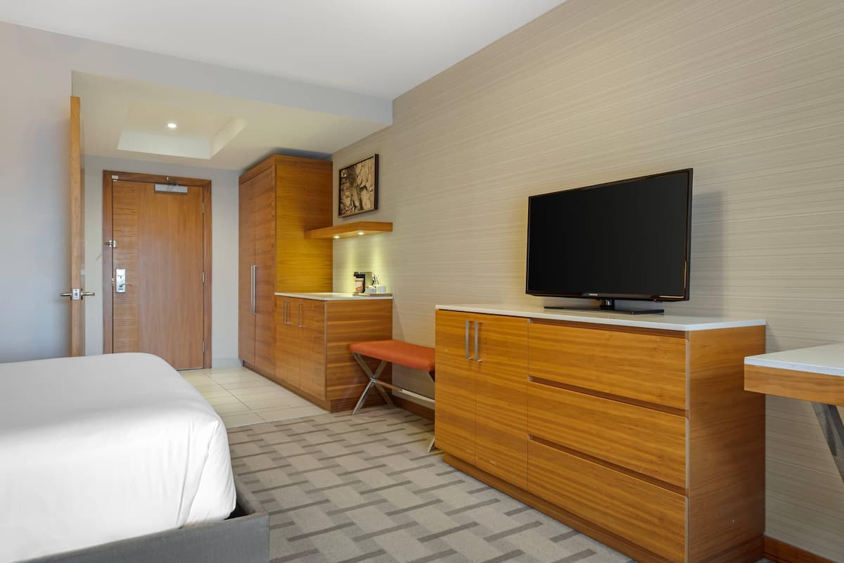 A hotel room with a bed, wooden wardrobe, a television, and a small table.