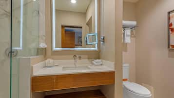 A modern bathroom with a glass shower enclosure, a wooden vanity, a white sink, and a toilet.