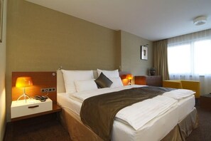 Una habitación de hotel con una cama grande, dos mesitas de noche con lámparas, un escritorio pequeño y una silla.