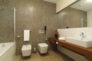 Un baño moderno con pared de mosaicos, un lavabo grande, un bidé y un inodoro.