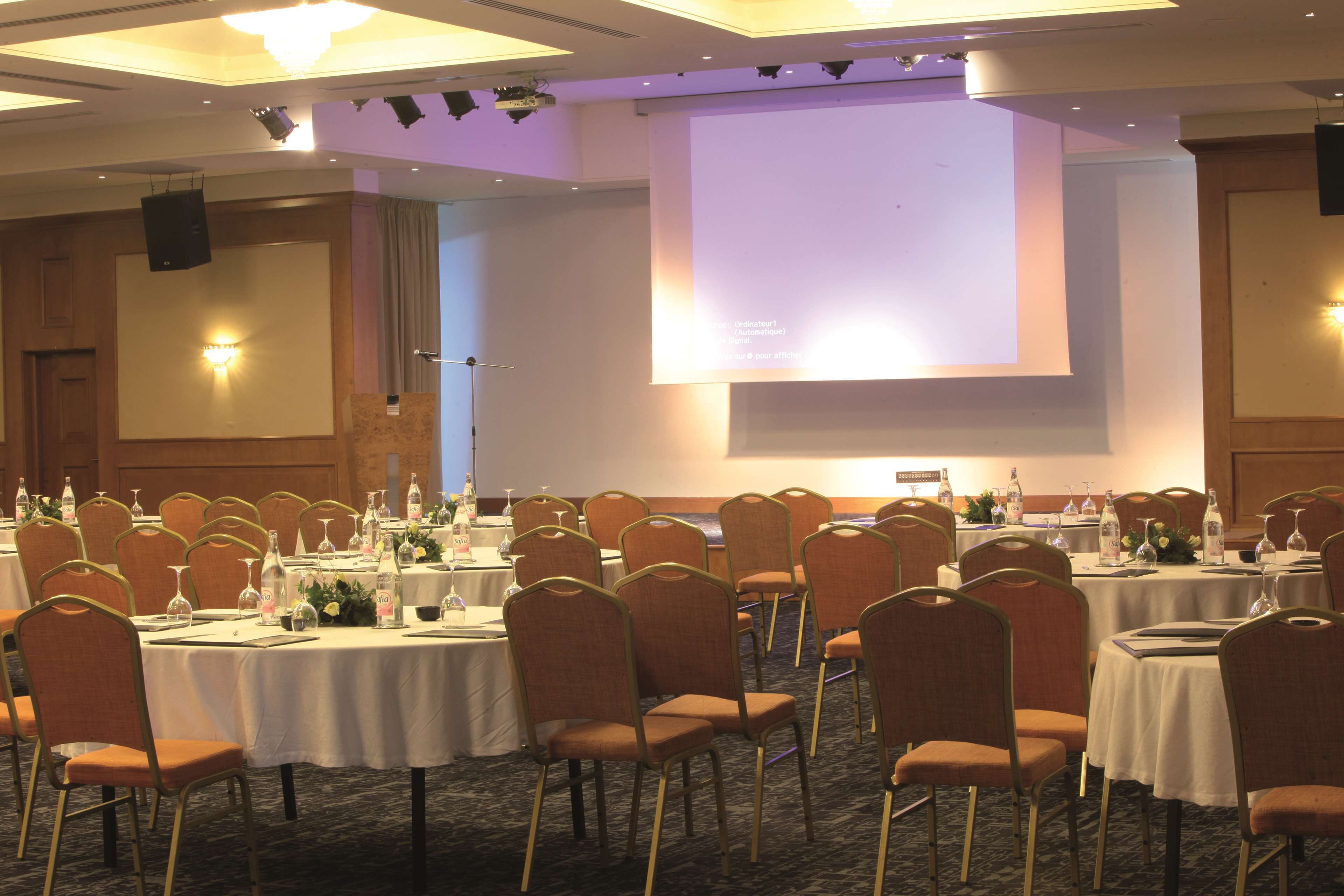 Een congrescentrum met ronde tafels, stoelen en een groot scherm voor presentaties.