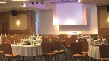 Een congrescentrum met ronde tafels, stoelen en een groot scherm voor presentaties.