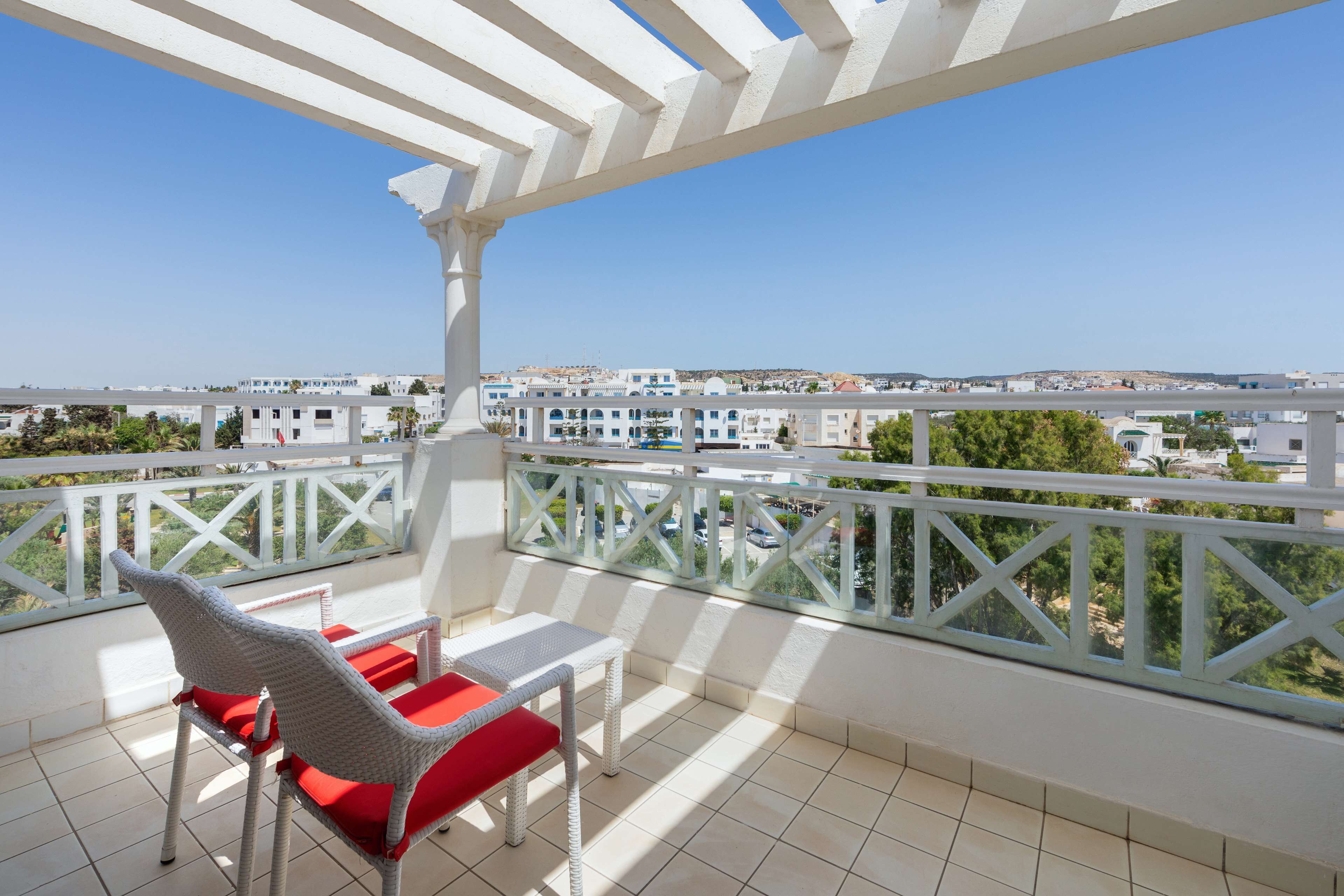 A balcony with a white railing, a wicker chair with a red cushion, and a small table.