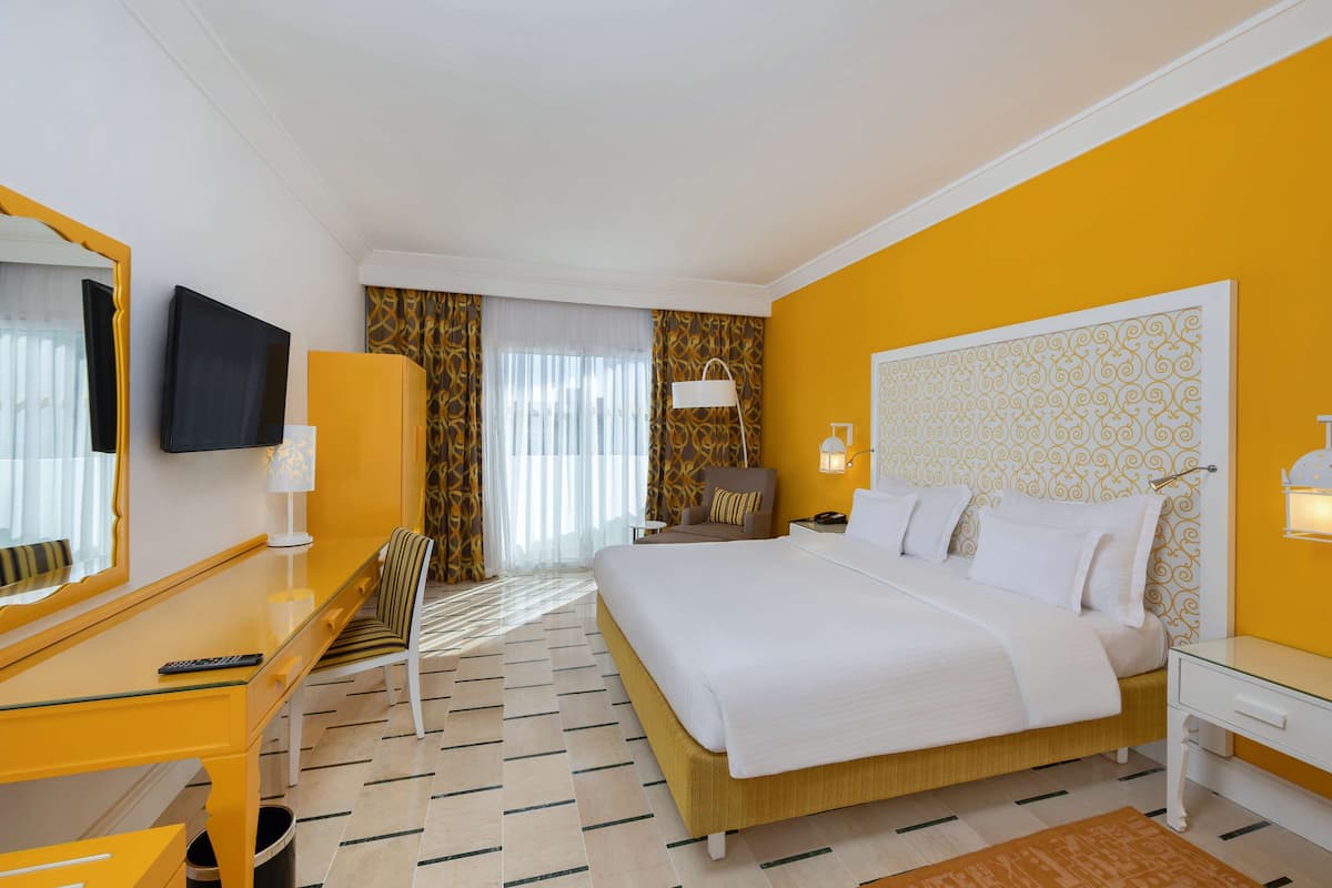 Une chambre d’hôtel avec un lit, un bureau, une chaise, une télévision et une fenêtre avec des rideaux.