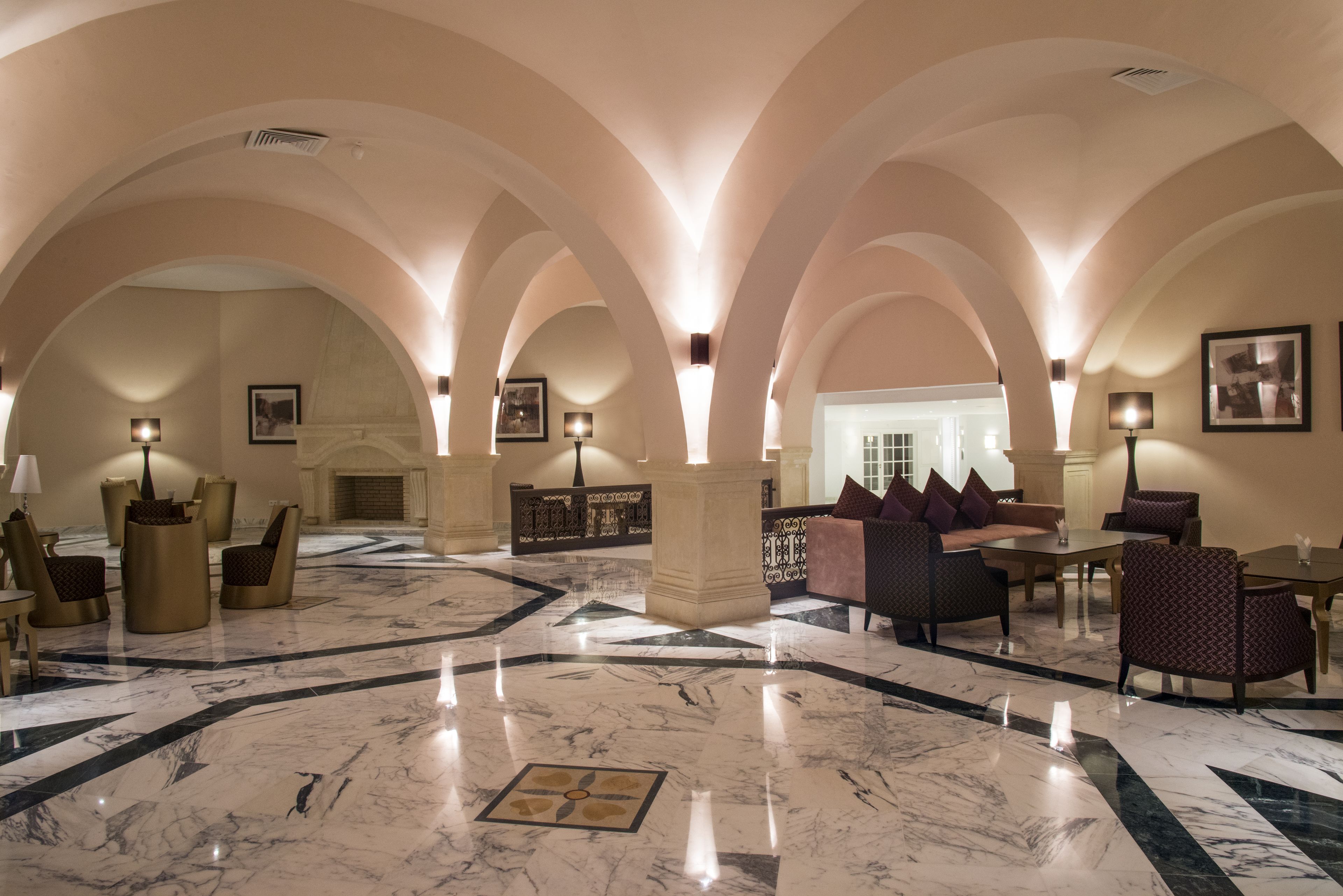 Un hall d’entrée doté de plafonds voûtés, de revêtements de sol en marbre et d’espaces aménagés avec des tables et des chaises.