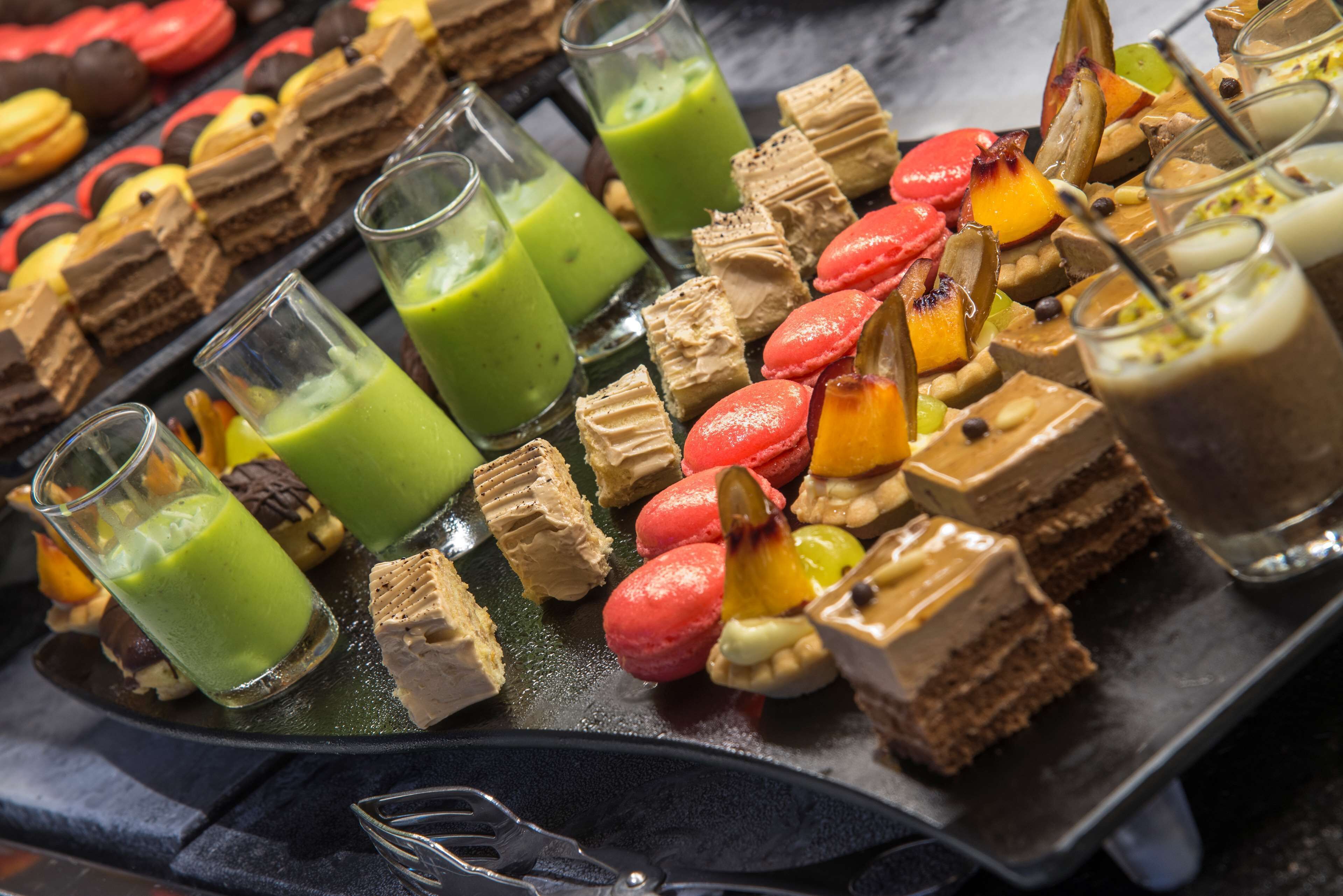 Un assortiment de desserts, notamment des macarons, des gâteaux et des boissons, présentés sur un plateau.
