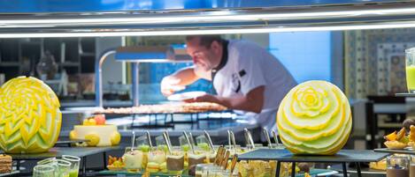 Un bufé con diversas opciones de comida y un chef preparando alimentos al fondo.