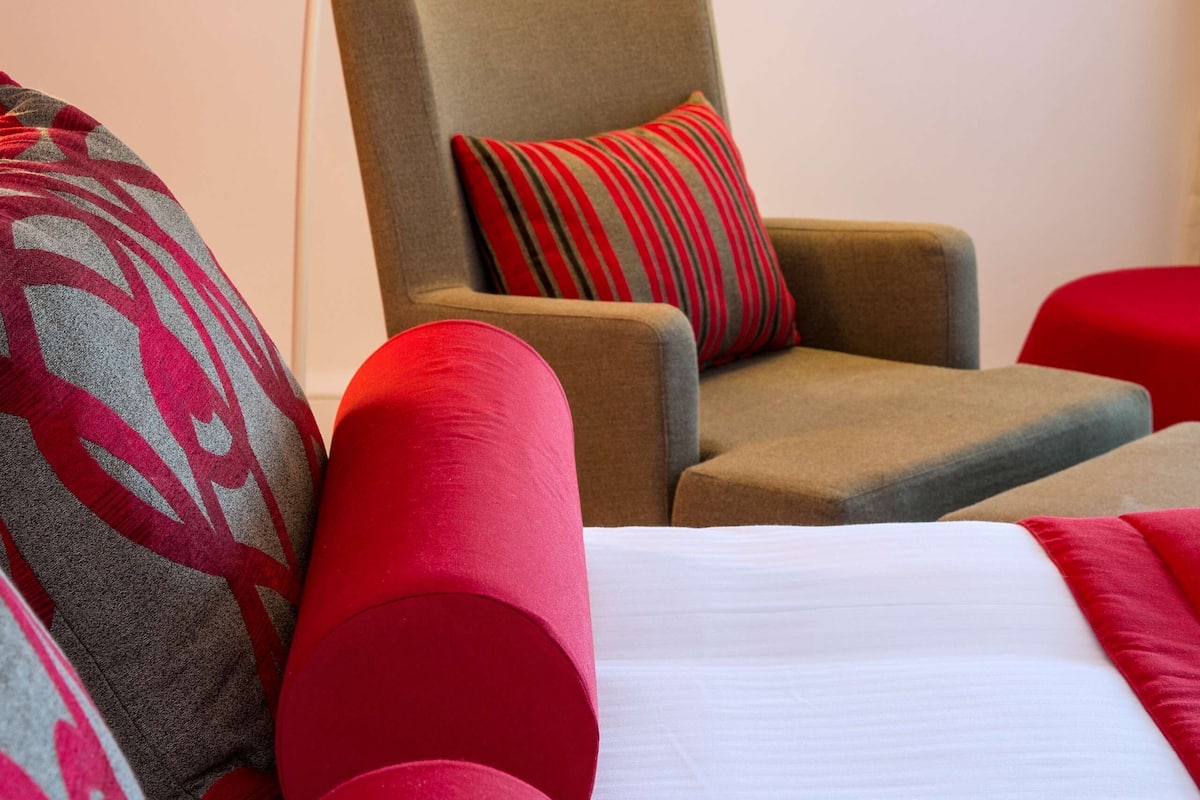 A hotel room with a bed, a chair, and a decorative light fixture.