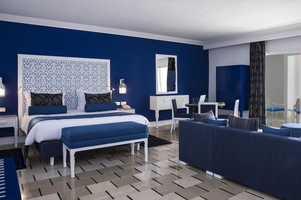 A hotel room with a bed, a sofa, a desk, and a view of the sea.