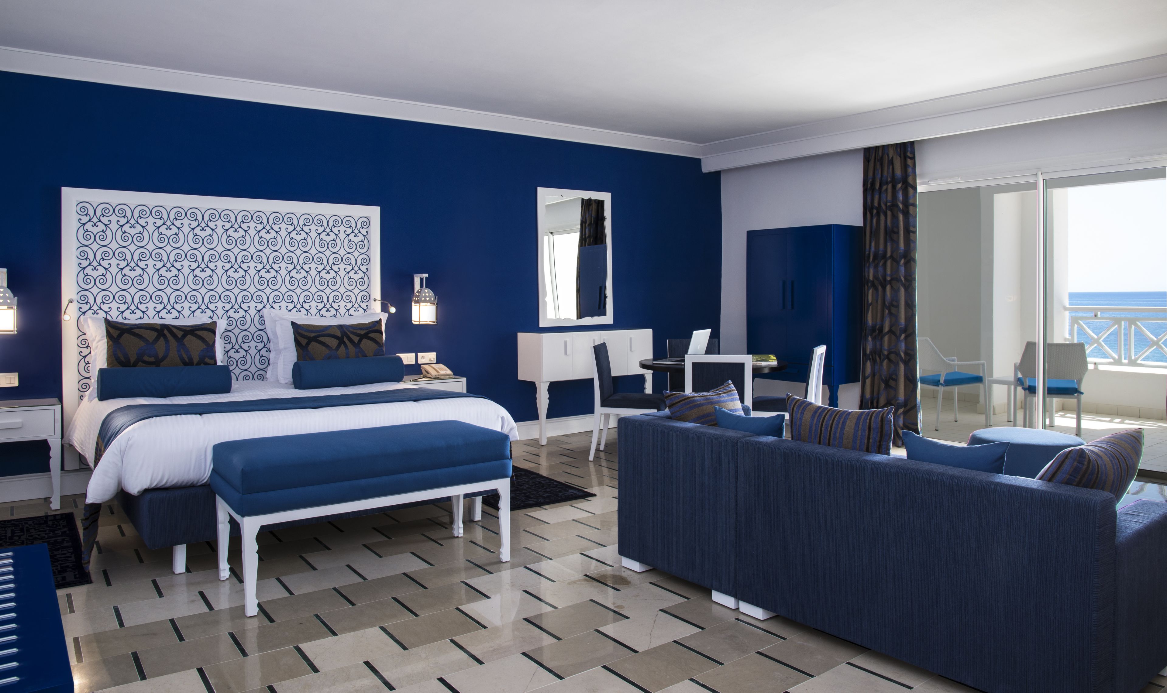 Habitación de hotel con cama, escritorio, sillón, sofá y vista al mar.