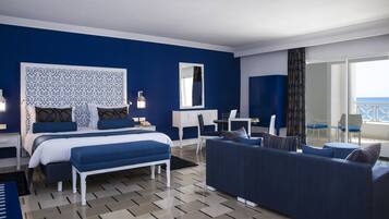 Habitación de hotel con cama, escritorio, sillón, sofá y vista al mar.
