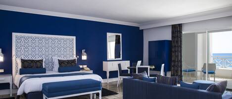 A hotel room with a bed, a desk, a chair, a sofa, and a view of the sea.
