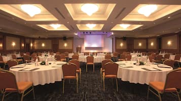 Un amplio salón de conferencias con mesas redondas, sillas y un escenario con una pantalla.