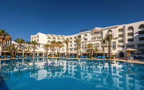 Ein Hotel mit großem Pool, Palmen und blauen Liegestühlen.