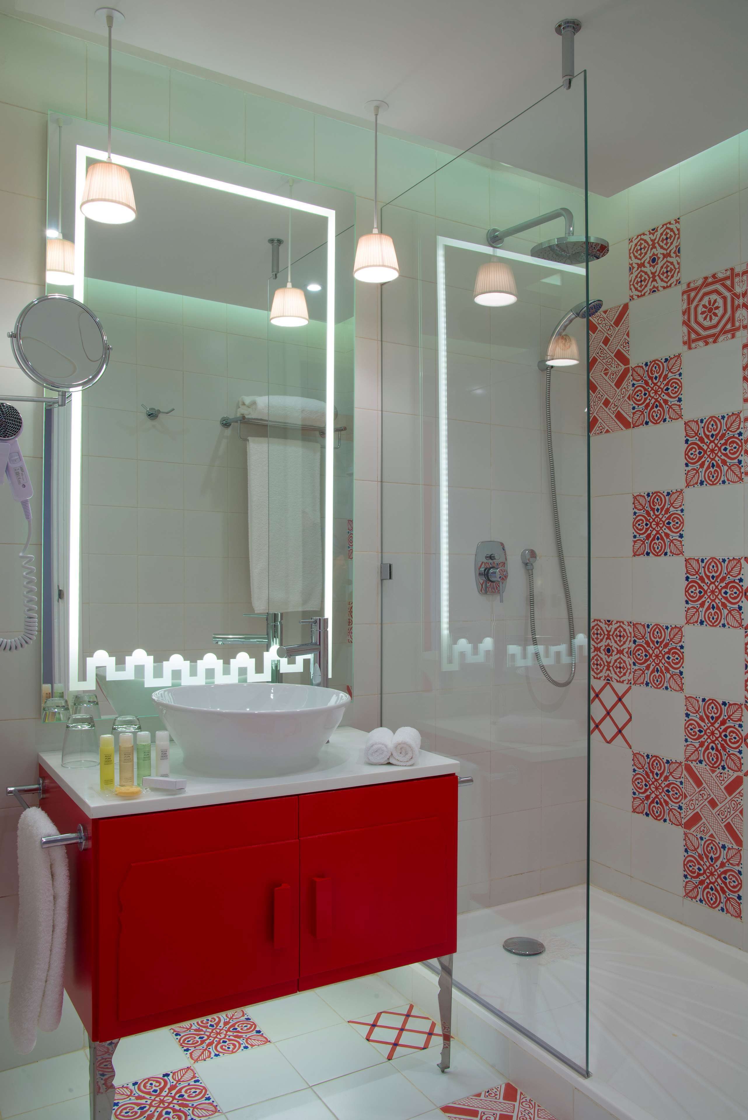 A modern bathroom with a large mirror, red vanity, glass shower enclosure, and patterned tiles.