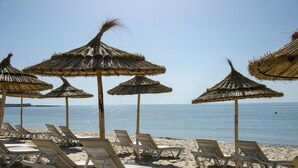 Una playa con sombrillas de paja y sillones blancos.