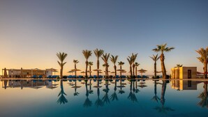 A pool area with lounge chairs and umbrellas, palm trees, and a pool bar. - Radisson Blu Resort & Thalasso, Hammamet (Hammamet)