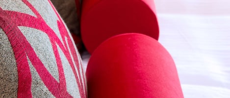 A bed with red and grey patterned pillows, a brown armchair with a striped pillow, and a red cylindrical pillow.