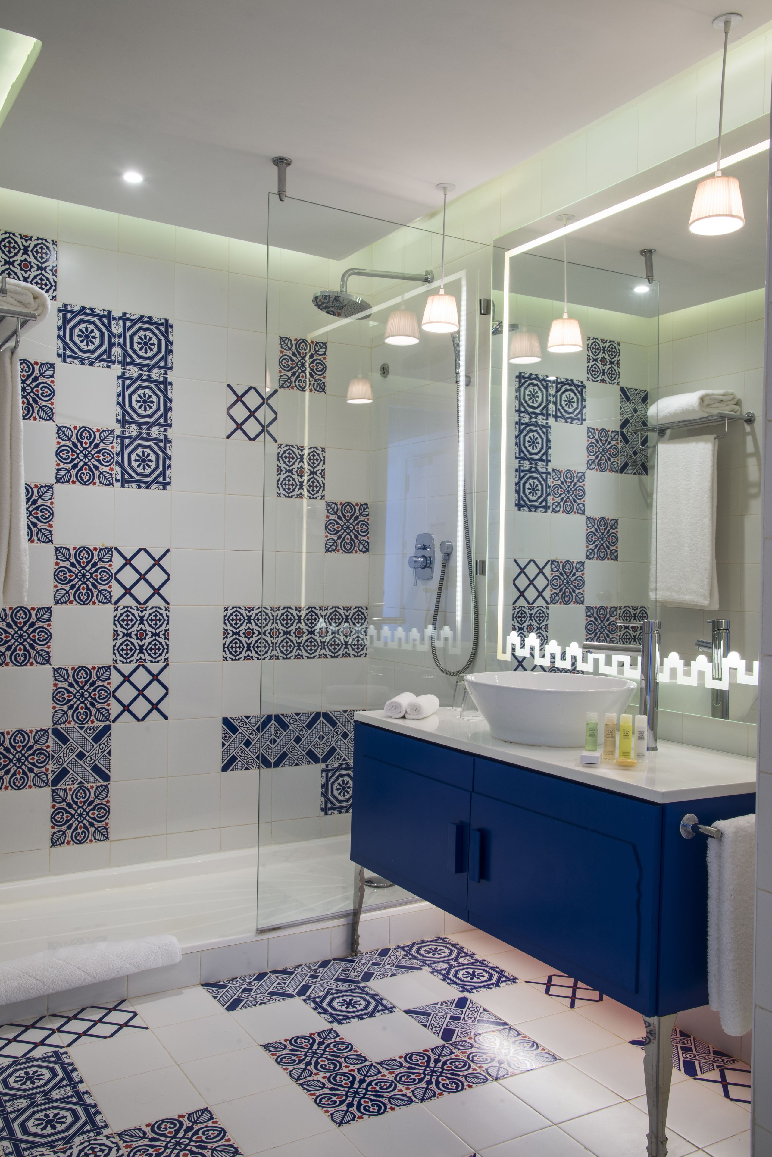 A modern bathroom with a glass shower enclosure, a blue vanity, and patterned tiles.