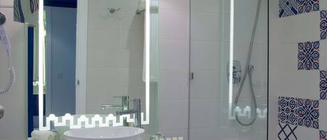 Un baño moderno con un espejo grande, armarios azules, cerramiento de ducha de vidrio y azulejos estampados.