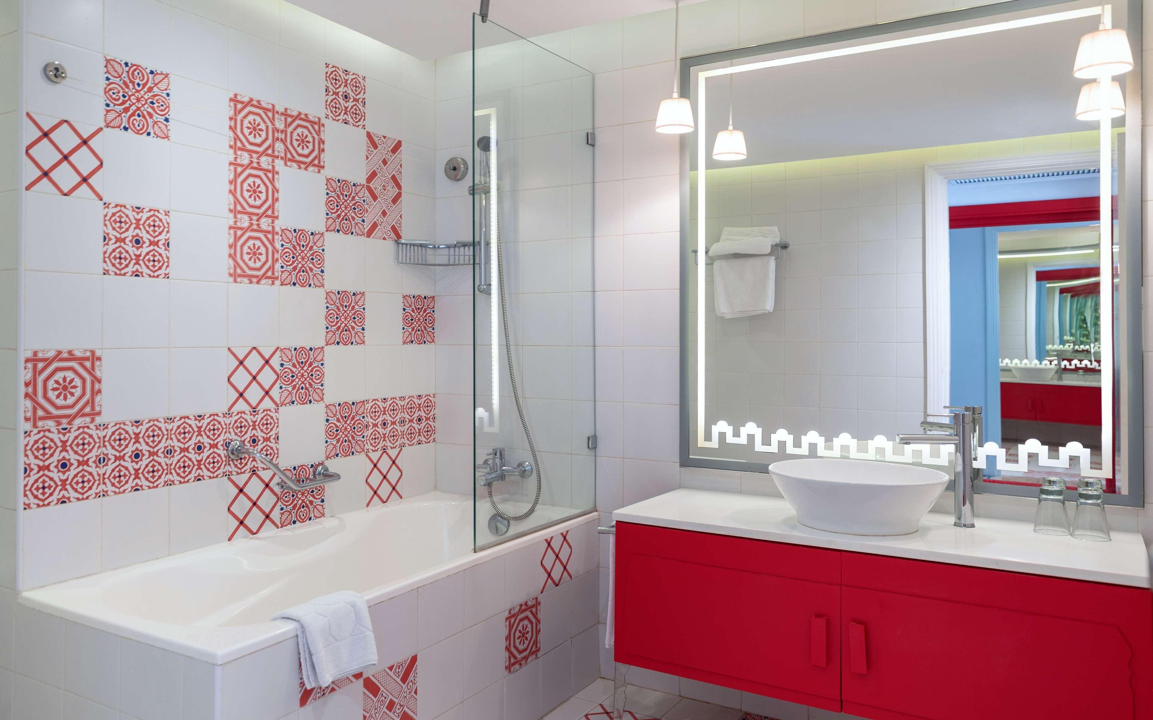 A modern bathroom with a white bathtub, red vanity, and patterned tiles.