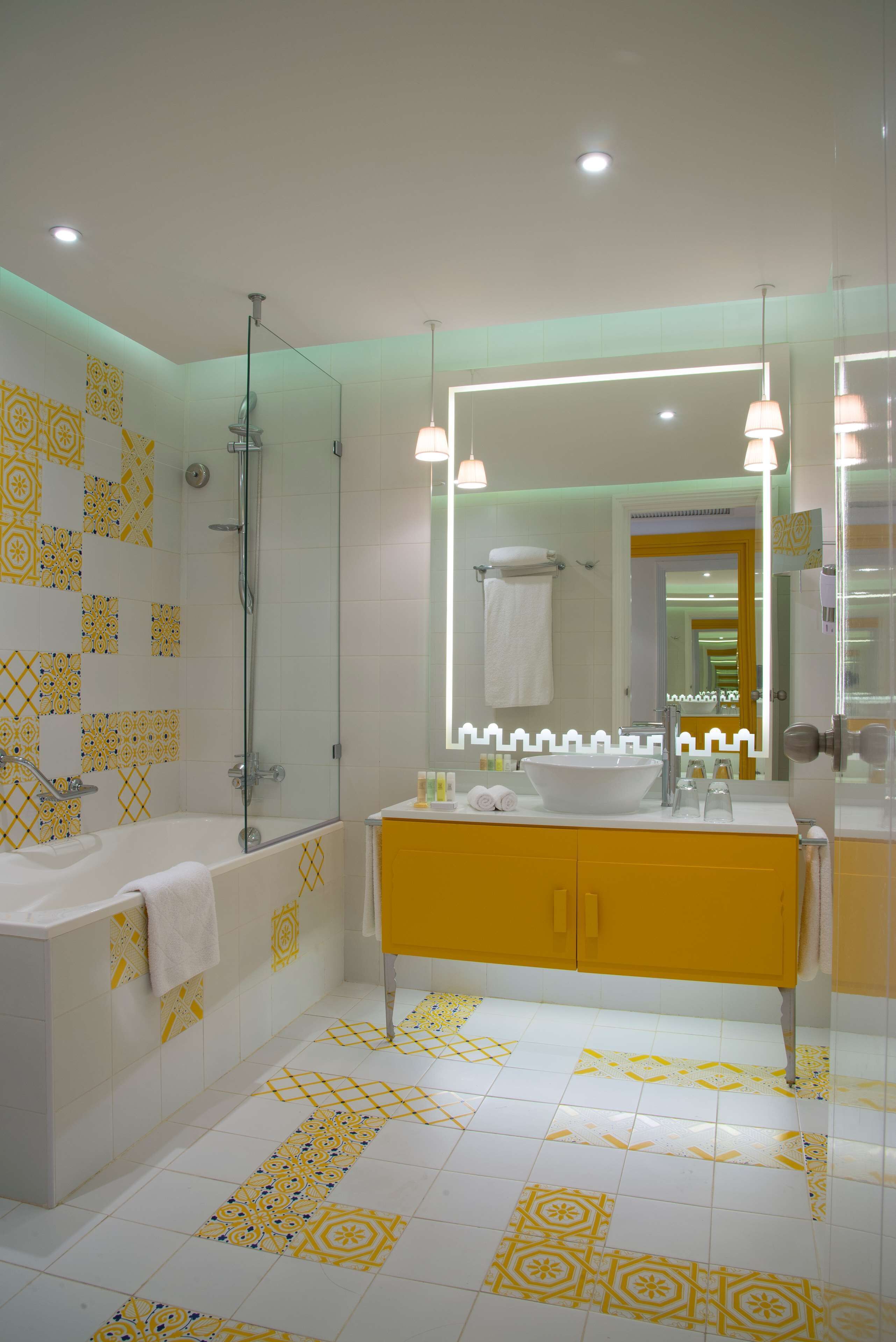A bathroom with a bathtub, a sink with a mirror, and patterned tiles on the walls and floor.