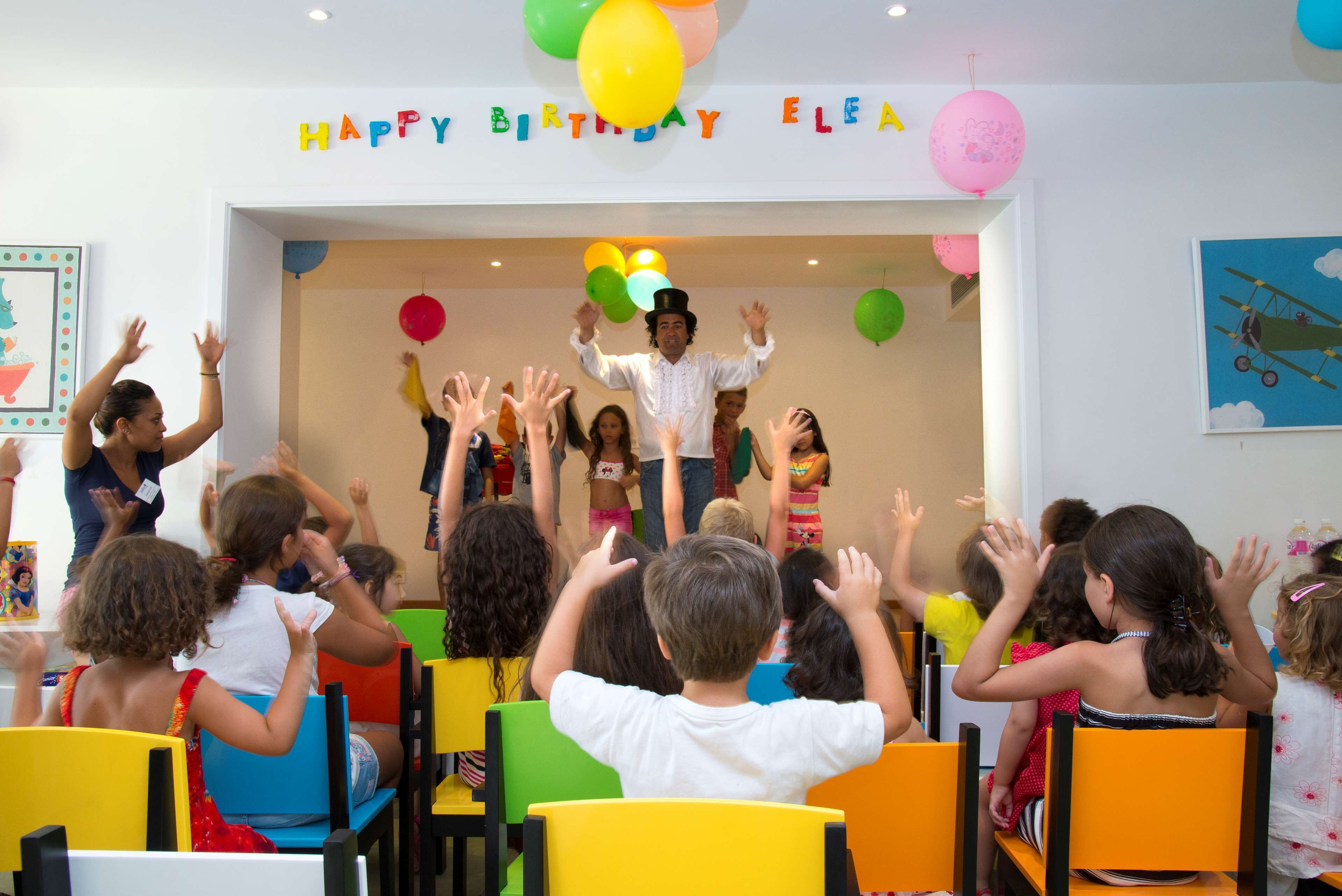 A classroom with children seated and a teacher standing at the front.