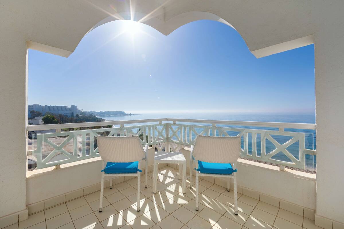 Un balcon avec deux chaises en osier blanc, un sol carrelé et une balustrade blanche.