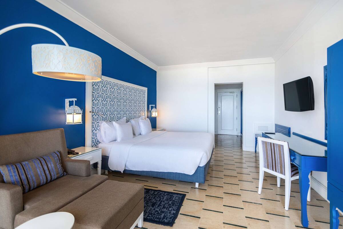 Une chambre d’hôtel avec un lit, un bureau, une télévision et un mur d’accent bleu.